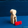 A wooden figure of a female with a void from which a red child like figure fell, showing the concept of abortion or miscarriage.