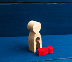 A wooden figure of a female with a void from which a red child like figure fell, showing the concept of abortion or miscarriage.